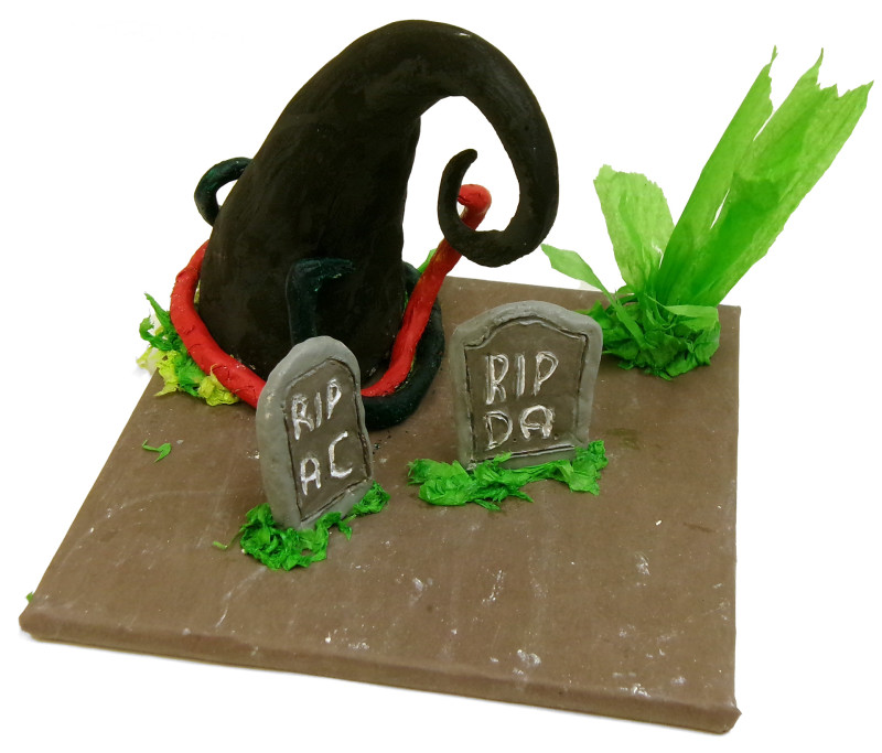 A tabletop sculpture focused on two gravestones. The graves read 