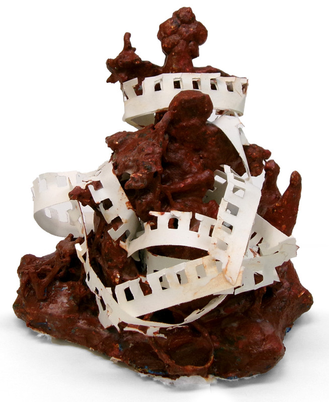 An abstract sculpture of a turd-like shape, with the edges of notebook paper encased within.