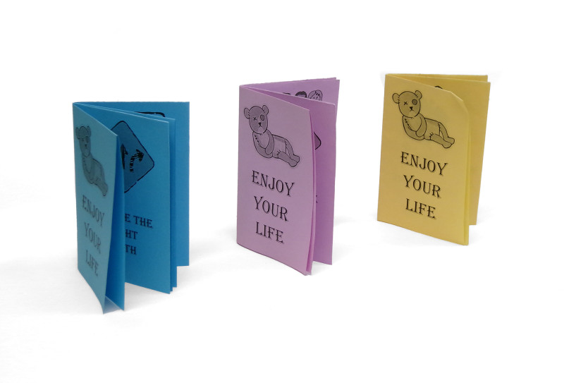 Three small booklets photographed in a diagonal line. One is bue, one purple, and one yellow. Eahc has the same cover, a supine, frowning teddy bear with one eye above the text 